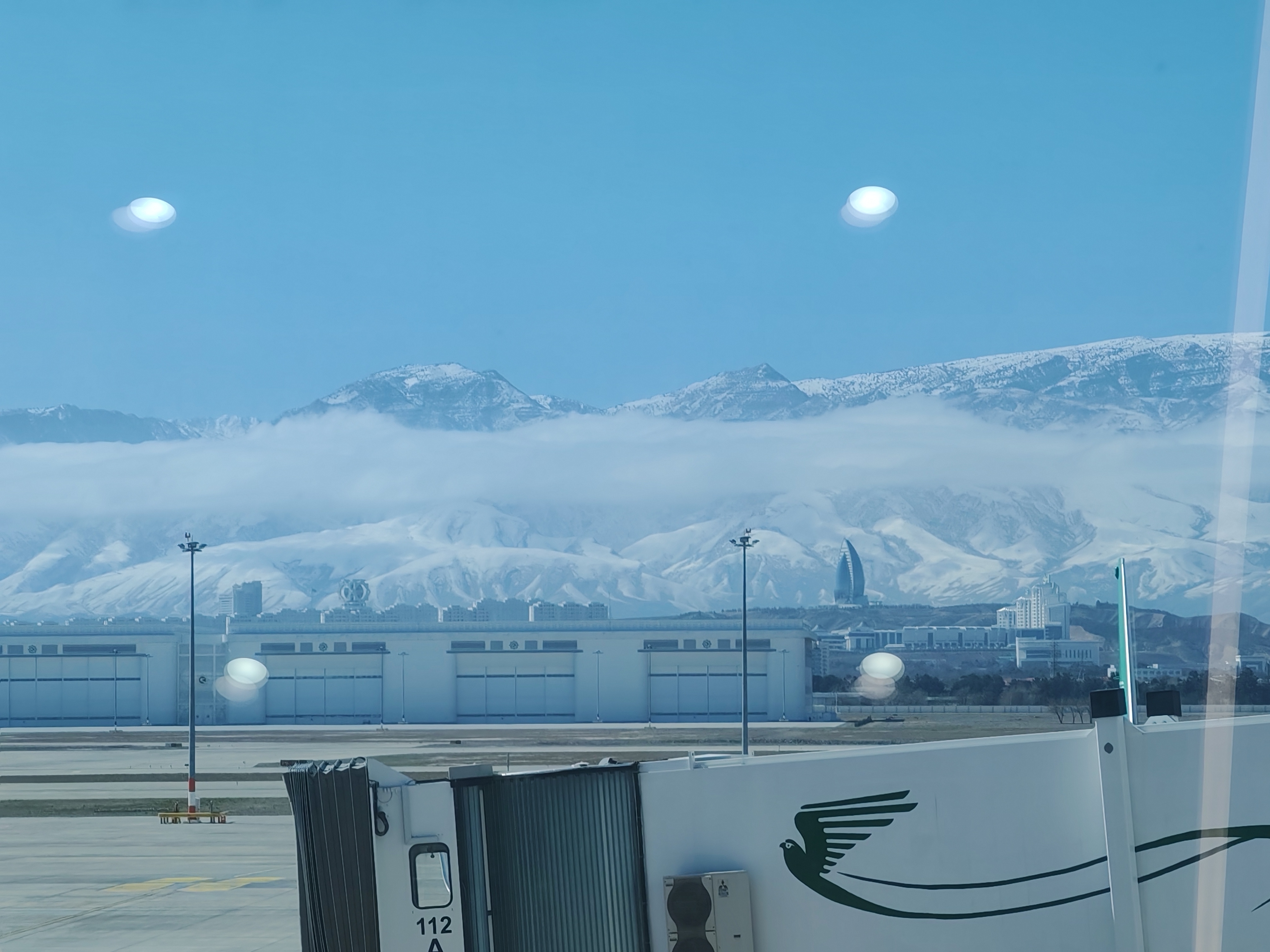 Luftaufnahme der weissen Marmorskyline von Aschgabat mit dem Kopet-Dag-Gebirge im Hintergrund bei goldenem Licht, aufgenommen vom Internationalen Flughafen Aschgabat